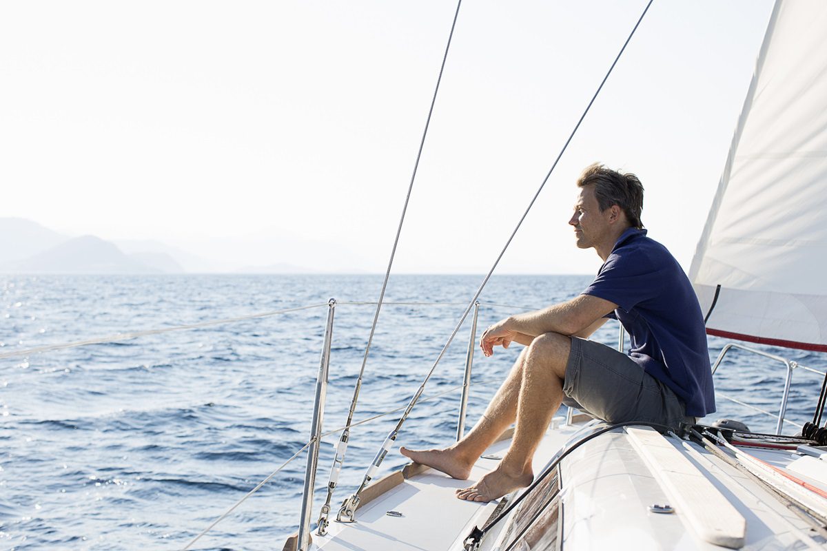 A man sits barefoot on the deck of a sailboat