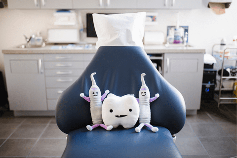 A dental chair with two toothbrush plush toys and a tooth plush toy placed on the seat in a dental office setting.