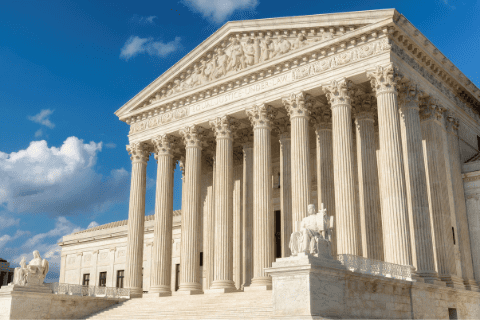 The front facade of the United States Supreme Court building with tall columns and statues under a partly cloudy sky.
