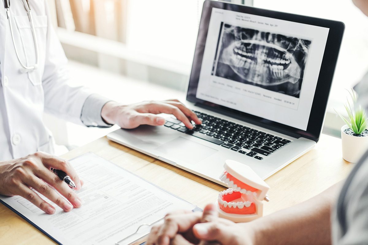 A dentist reviews a dental x-ray on a laptop with a patient