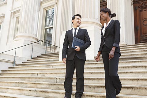 Two business professionals in suits walk and talk on the steps outside a large