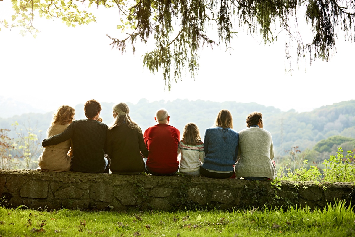 Rear view of multi-generation family relaxing in row on retaining wall against clear sky